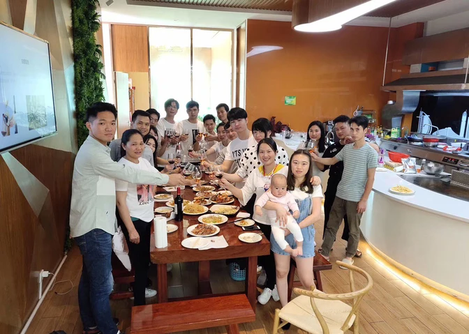 A collaborative group of people pose for a photo around a dining table set with various dishes in a modern kitchen. A woman holds a baby in her arms.