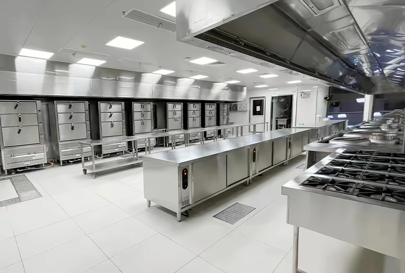 A modern, stainless steel commercial kitchen equipped with high-end cooking equipment, multiple ovens, stoves, and spacious preparation areas under bright lighting.