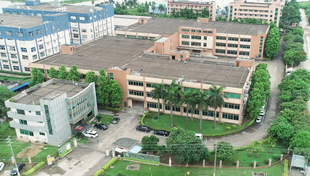 Aerial view of a commercial building complex with multiple structures, trees, and parked vehicles. The buildings have beige and blue exteriors, offering a first look at the area that feels almost like home due to the abundant greenery surrounding it.