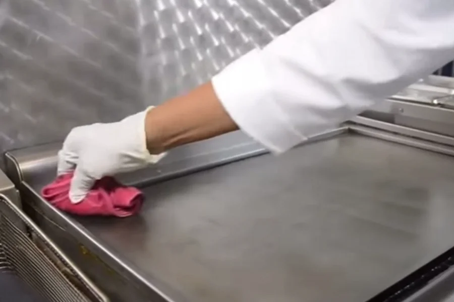 The staff is carefully wiping the stainless steel commercial clamshell griddle.