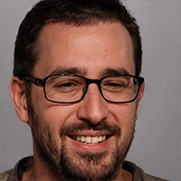 A man with short dark hair, a beard, and glasses is smiling. He is wearing a casual top and is positioned against a plain background, perhaps dreaming of Island Cooking Suites for his next culinary adventure.