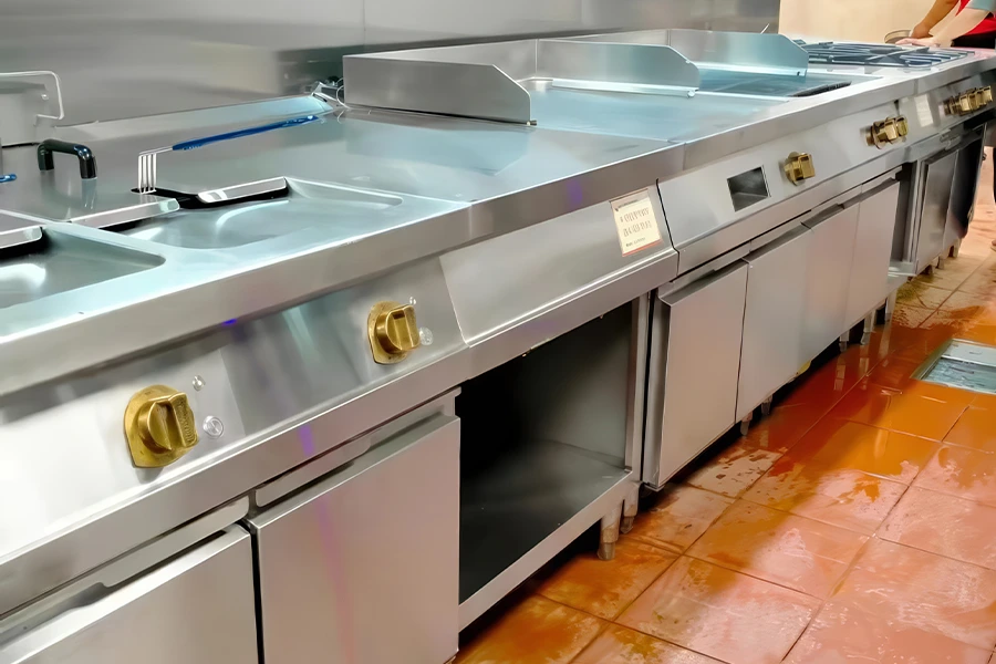 A commercial kitchen with stainless steel appliances, including commercial griddles, fryers, and stovetops, on a clean, red-tiled floor.