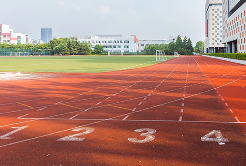 A four-lane running track in a sports field with buildings in the background on a clear day, guaranteeing an excellent environment for athletic training.