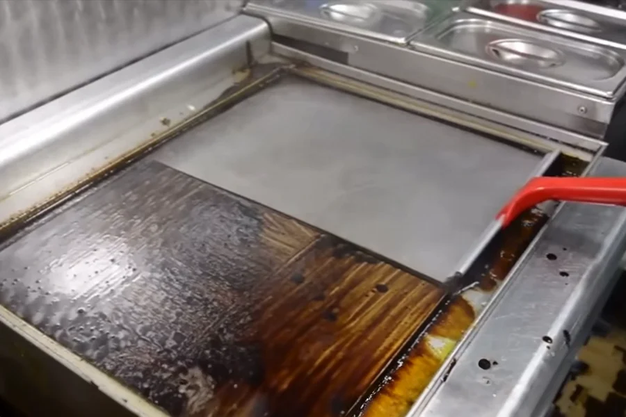 Cleaning a greasy and dirty commercial clamshell griddle with a spatula