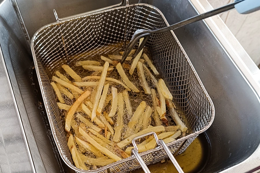 French fries are being deep-fried in a wire basket immersed in hot oil inside a commercial deep fryer.