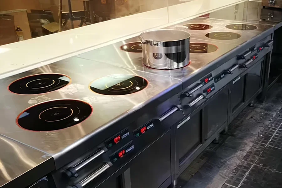 A commercial kitchen with multiple induction cooktops, including a commercial induction cooker, one of which is currently in use, heating a pot.