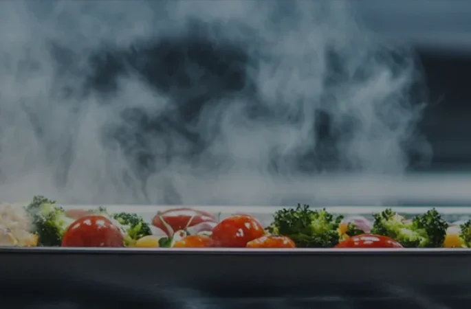 Commercial cooking equipment is used to cook fresh vegetables and meats, with steam rising from the pot, showing the colorful ingredients and the cooking process.