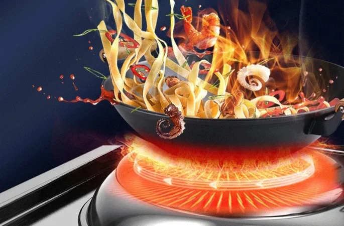 Flames rise from the red-hot commercial chinese induction wok range, tossing noodles, shrimp and vegetables into the air.