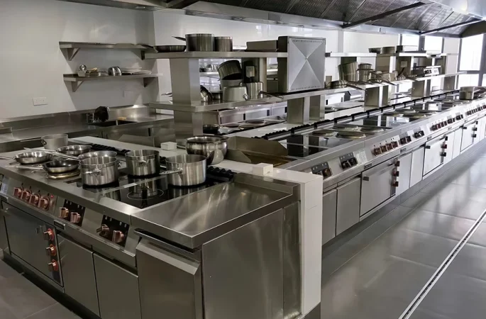 Commercial kitchen with stainless steel cooking equipment, including stoves, ovens, and cookware arranged neatly on countertops and shelves