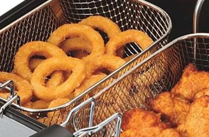 Fried onion rings and breaded chicken pieces sizzling to perfection in the baskets of a commercial deep fryer.