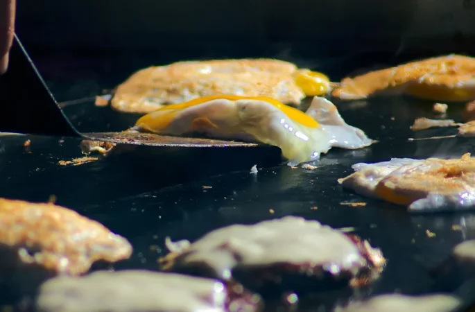 Close-up showing several fried eggs being cooked on a induction griddle. The eggs with still runny yolks indicate that cooking is still in progress.